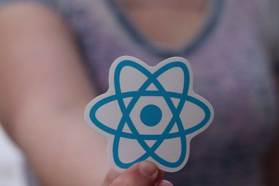A person holding a sticker featuring a blue and white atomic model design, with a central circle and interlinked curved lines representing electrons orbiting the nucleus, in front of a blurred backgro
